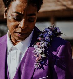 a man in a purple suit and flower boutonniere looks down at his watch