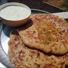 two flat breads on a plate next to a bowl of yogurt