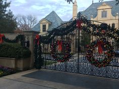 an iron gate decorated with christmas wreaths and ornaments in front of a house on a cloudy day