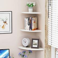 a corner desk with a computer, clock and flowers on it in front of a window