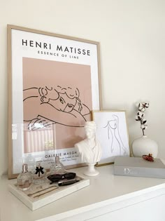 a white shelf topped with perfume bottles next to a vase and framed artwork on top of it