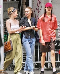 three young women walking down the street talking to each other and one is wearing a red hat