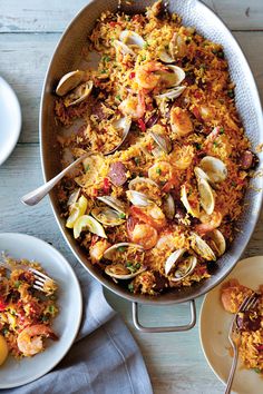 a pan filled with rice and clams next to plates of food on a table