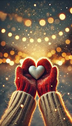 someone's hands holding a heart in front of a boke of lights and snow