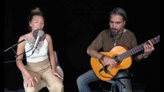 a man and woman sitting next to each other while playing guitars in front of microphones