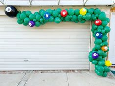 an arch made out of balloons with pool balls on it in front of a garage