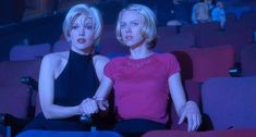 two women sitting in the middle of a movie theater, one with her hand on another's shoulder