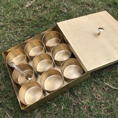 an open box filled with lots of empty bowls on top of green grass next to a metal spoon