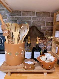 kitchen utensils are in a clay container on a wooden tray next to bottles