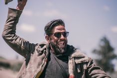 a man with sunglasses and a beard holds up a bird in the air above his head