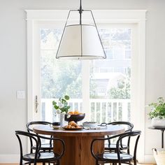 a dining room table with four chairs and a bowl of fruit on it in front of a window