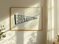 a framed boston pennant hangs on the wall next to a potted plant and window