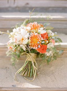 an orange and white bouquet with greenery tied to it's side on a stone wall