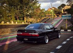 a black car parked on the side of a road next to a colorful wall and stairs