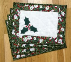 three quilted placemats with holly designs on them sitting on a wooden floor