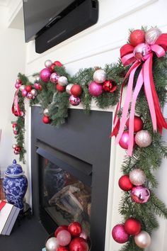 a fireplace decorated for christmas with red, white and pink ornaments around the mantel