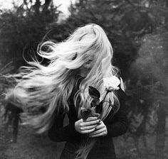 a woman with long hair holding a flower in her hand and blowing it into the wind