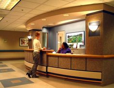 a woman is standing at the front desk of a hotel reception area with two people