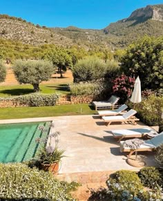 an outdoor swimming pool with chaise lounges and mountains in the background on a sunny day