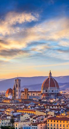 the city skyline is shown at sunset with clouds in the sky and mountains in the background