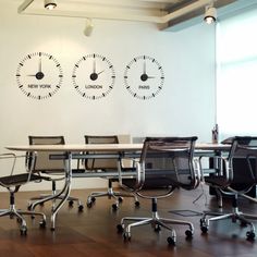 an empty conference room with three clocks on the wall and four chairs in front of it