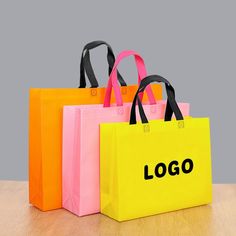 three shopping bags with the word logo printed on them sitting on a wooden table in front of a gray background