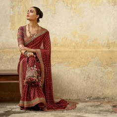 a woman in a red sari sits on a bench and looks off into the distance