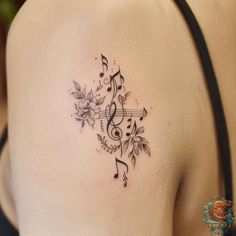 a woman's shoulder with music notes and flowers tattoo on her left side ribcage