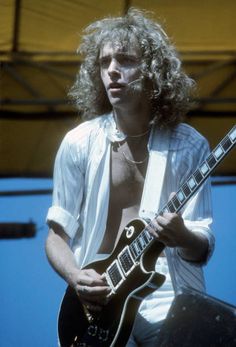 a man with long hair plays an electric guitar on stage at a music festival or concert