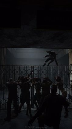 a group of people standing in front of a metal fence at night with the lights on