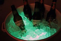 four bottles of beer are sitting in an ice bucket with green lights on the bottom