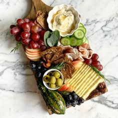 an assortment of cheeses, crackers, and fruit on a wooden platter