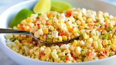 a white bowl filled with corn salad next to a green apple and lime wedges