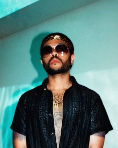 a man with tattoos and sunglasses on standing in front of a wall wearing a black shirt