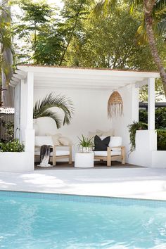 an outdoor living area next to a pool with lounge chairs and potted palm trees