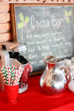 a red table topped with candy canes and a silver pitcher next to a chalkboard