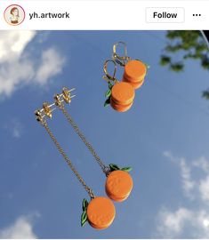 three oranges hanging from chains on a blue sky with clouds in the back ground