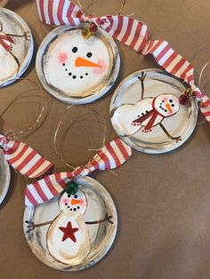 four snowman ornaments are hanging on the table with red and white striped ribbon around them