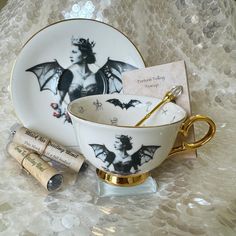 a tea cup and saucer with bat designs on it, next to some wine corks