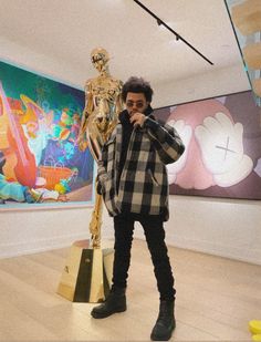 a man standing next to a golden statue in front of a wall with paintings on it