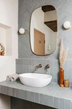 a bathroom sink sitting under a large mirror next to a vase with dry grass in it