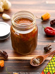 a jar filled with sauce sitting on top of a wooden table next to some vegetables