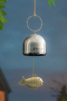 a metal bell with a fish hanging from it's side on a tree branch