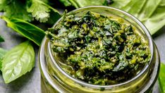 a jar filled with green pesto on top of a table next to some leaves