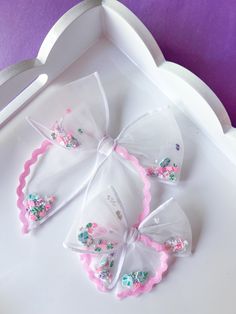 three small bows with pink and blue flowers on them sitting in a white tray next to scissors