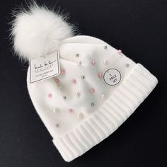 a white beanie with pink and white beads on it is sitting on a black surface