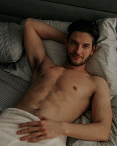 a shirtless man laying in bed under a blanket