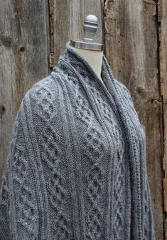 a gray knitted shawl sitting on top of a mannequin head next to a wooden fence