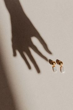 the shadow of a person's hand next to two small white and gold earrings