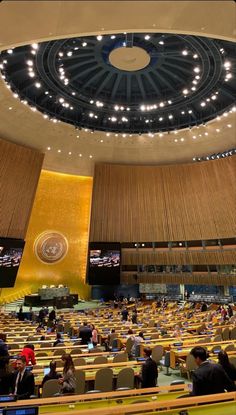 a large room filled with lots of people sitting at desks in front of a circular ceiling